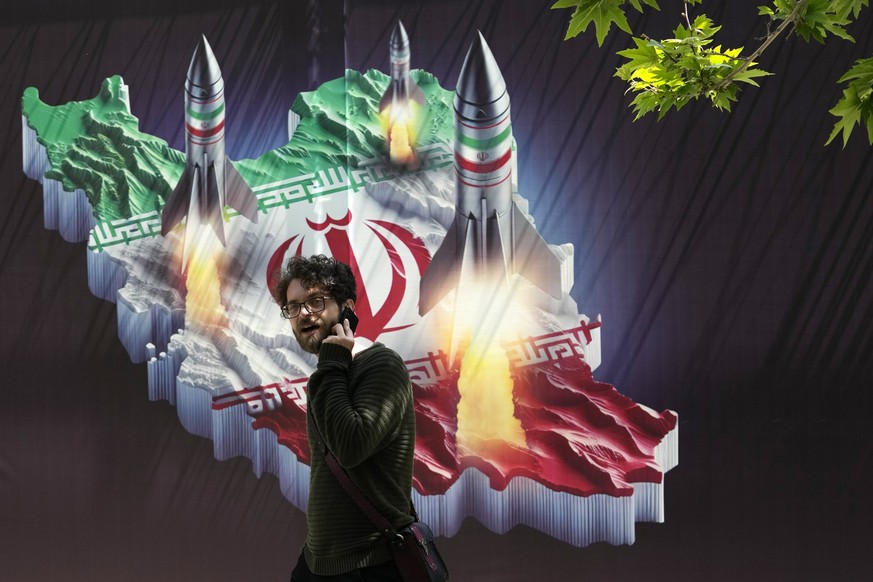 A passerby, taking on his cellphone, walks past a banner showing missiles being launched from Iranian map in northern Tehran, Iran, Friday, April 19, 2024. Iran fired air defenses at a major air base  ...