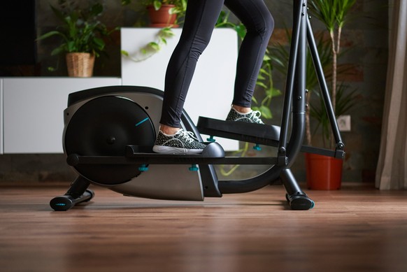 Woman legs training on smart elliptical trainer indoors at home in daylight with natural light