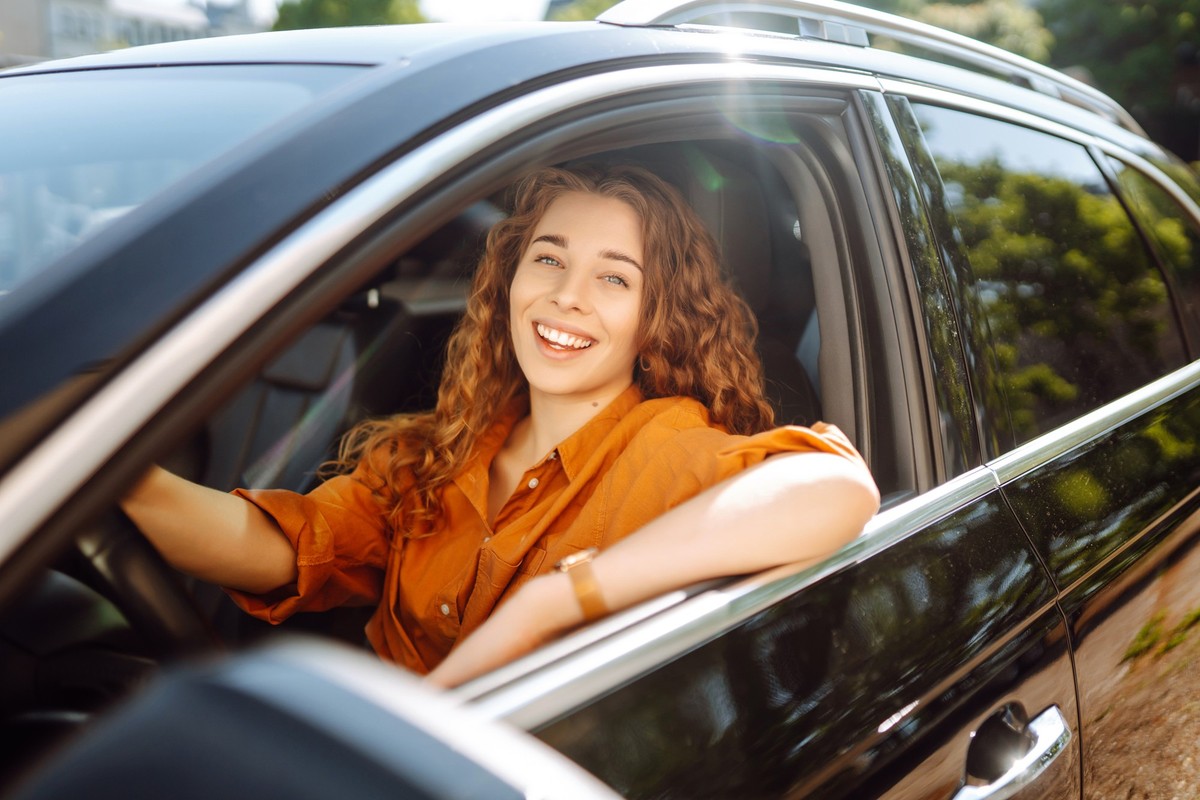Smiling woman driving a car. Attractive woman sitting in the driver&#039;s seat of a car. Outdoor portrait. The concept of transport, lifestyle.