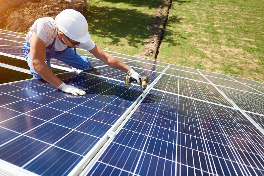 Professional worker installing solar panels on the green metal construction, using different equipment, wearing helmet. Innovative solution for energy solving. Use renewable resources. Green energy.