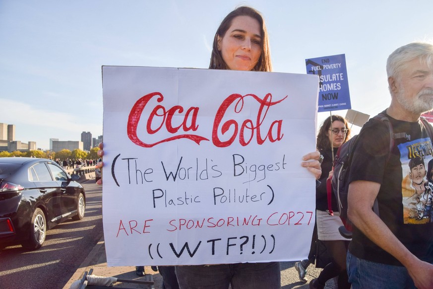 November 12, 2022, London, England, United Kingdom: A protester on Waterloo Bridge holds a sign opposed to Coca Cola sponsoring COP27. Thousands of people gathered outside Shell Headquarters in London ...