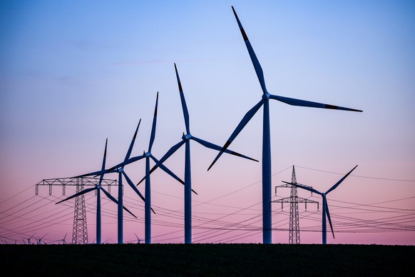ARCHIV - 04.10.2022, Sachsen-Anhalt, Leuna: Windkraftanlagen und Hochspannungsleitungen sind vor dem Abendhimmel bei Leuna zu sehen. Erneuerbare Energien haben in diesem Jahr mit rund 47 Prozent fast  ...