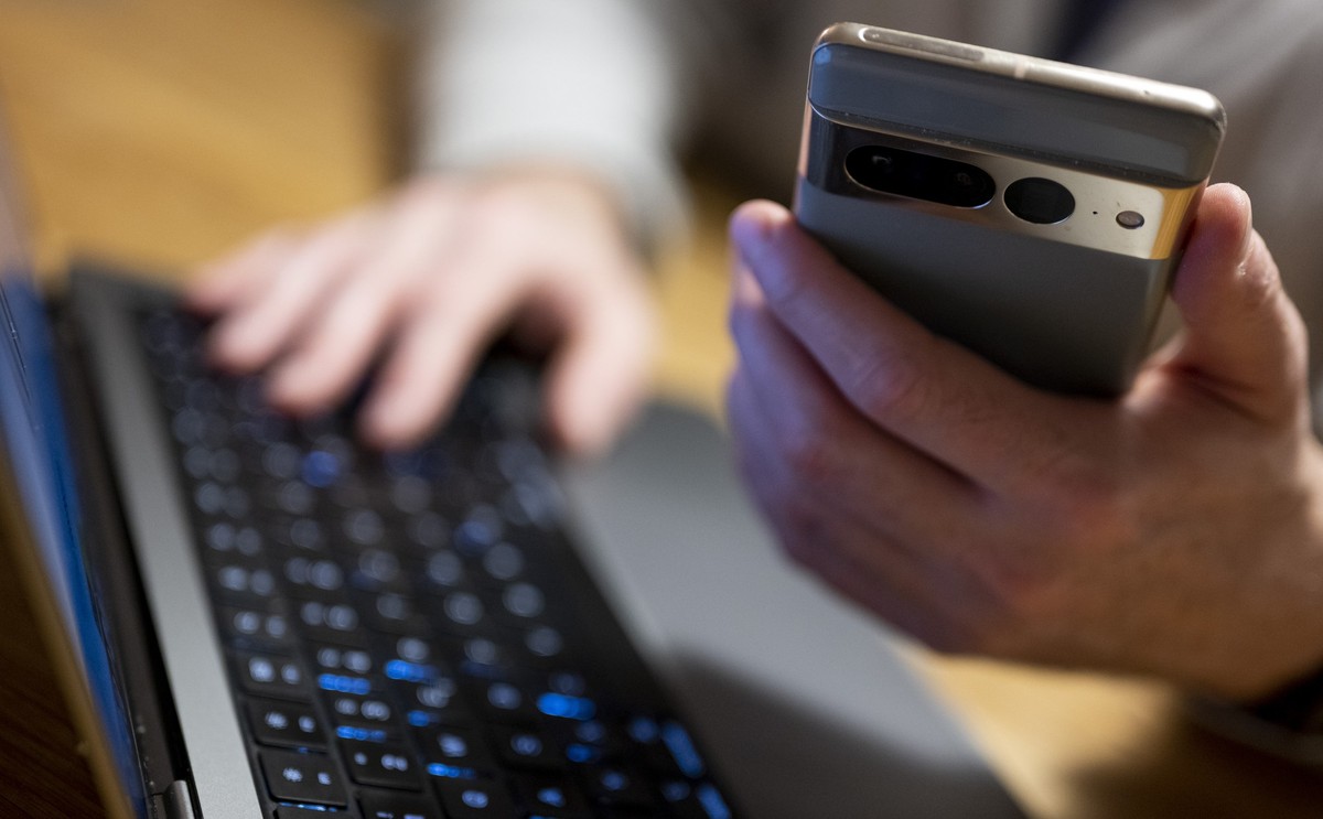 ILLUSTRATION - 27.02.2023, Berlin: Ein Mann sitzt am Laptop und h�lt ein Smartphone mit in der Hand. Der Digitalverband Bitkom sieht einen ungebrochenen Trend zum Online-Banking - inzwischen auch bei  ...