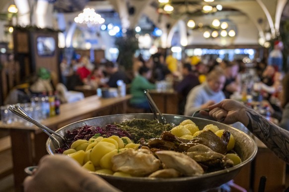 24.12.2022, Berlin: Eine Kellnerin tr�gt im Hofbr�u Berlin bei einem Weihnachtsessen eine Pfanne zum Tisch. Das christliche Kinder- und Jugendhilfswerk �Die Arche� hat insbesondere finanziell benachte ...