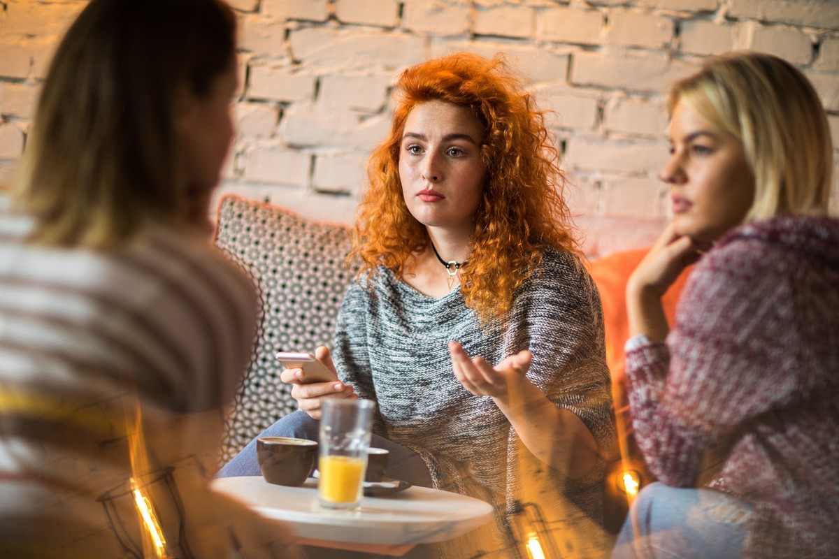 Worried redhead woman using cell phone while talking to her friends in a cafe.