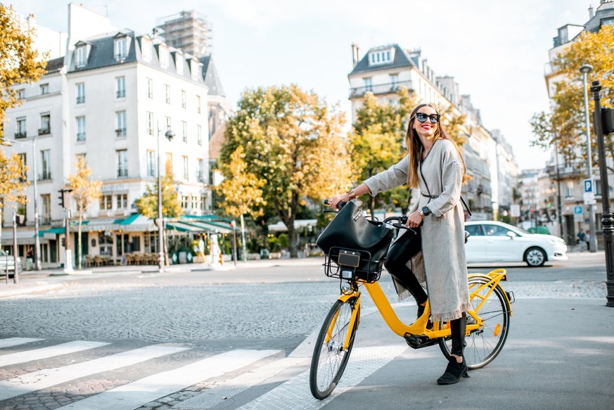 Portrait of a young stylish woman with yellow bicycle on the street in Paris