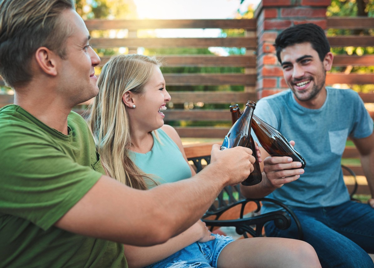 Friends, beers and backyard party with cheers for summer celebration and happy social hangout. Group of people laughing and toast together with beverage, drinks or alcohol bottle on patio at home Frie ...