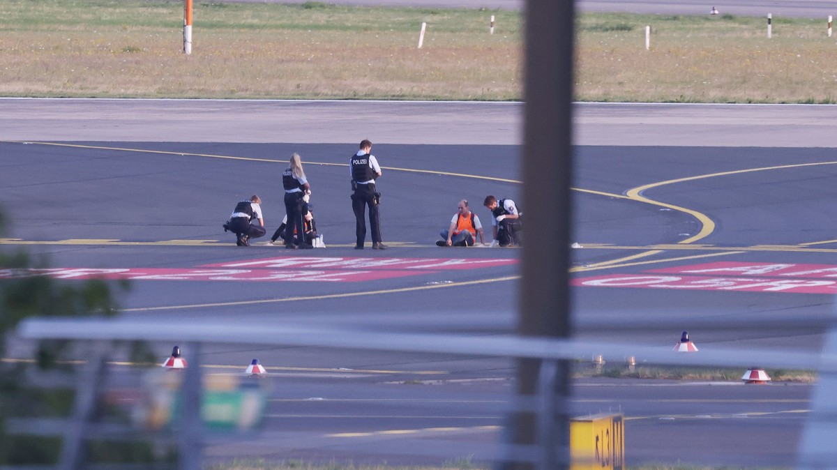dpatopbilder - 13.07.2023, Nordrhein-Westfalen, Düsseldorf: Polizisten stehen auf dem Flugfeld und versuchen Aktivisten der Gruppe Letzte Generation am Flughafen vom Asphalt zu lösen, nachdem sie sich ...