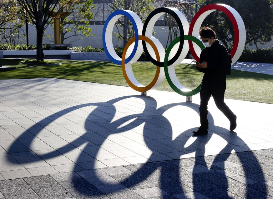Olympic symbol monument in Tokyo A man wearing a face mask walks past a monument depicting the Olympic rings in Tokyo s Shinjuku Ward on March 24, 2020. PUBLICATIONxINxGERxSUIxAUTxHUNxONLY