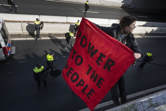 11.03.2023, Niederlande, Den Haag: Eine Demonstrantin der Gruppe «Extinction Rebellion» hält ein Transparent mit der Aufschrift &quot;Power to the people&quot; (&quot;Die Macht dem Volk&quot;), nachde ...