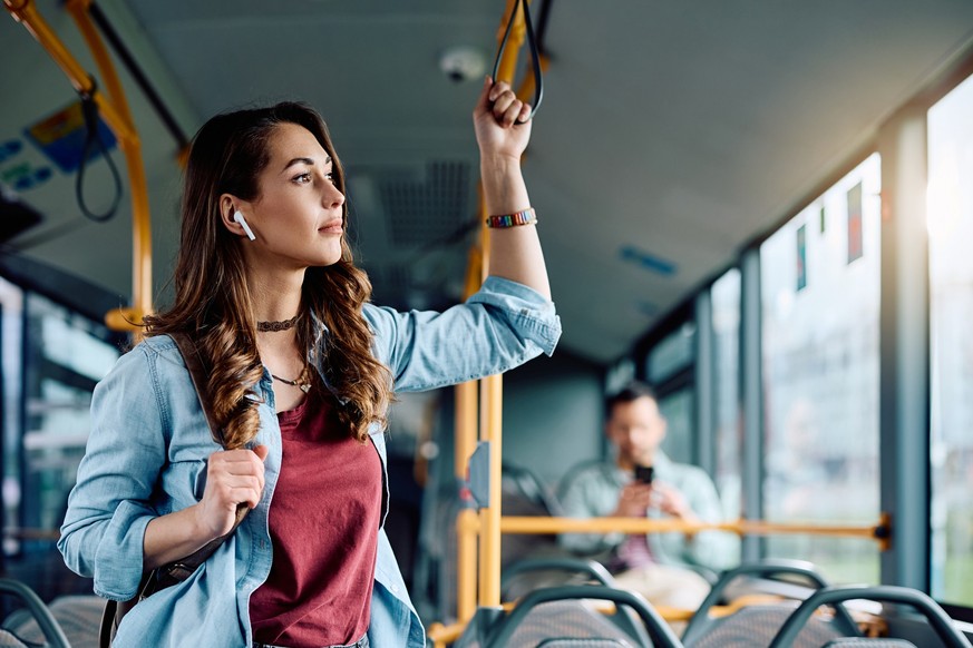 Young woman listening music over earbuds while commuting by city bus. Copy space.