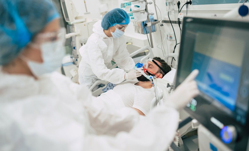 Coronavirus covid-19 infected patient in a quarantine ward at the hospital with doctors in protective suits while they making disease treatment of him