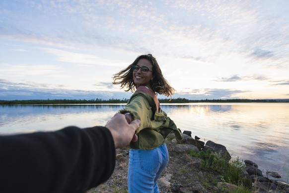 Finland, Lapland, happy young woman holding man s hand at the lakeside at twilight model released Symbolfoto PUBLICATIONxINxGERxSUIxAUTxHUNxONLY KKAF02321