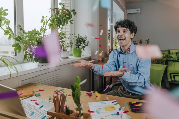 Excited businessman playing with confetti at desk in office model released, Symbolfoto property released, YTF01923