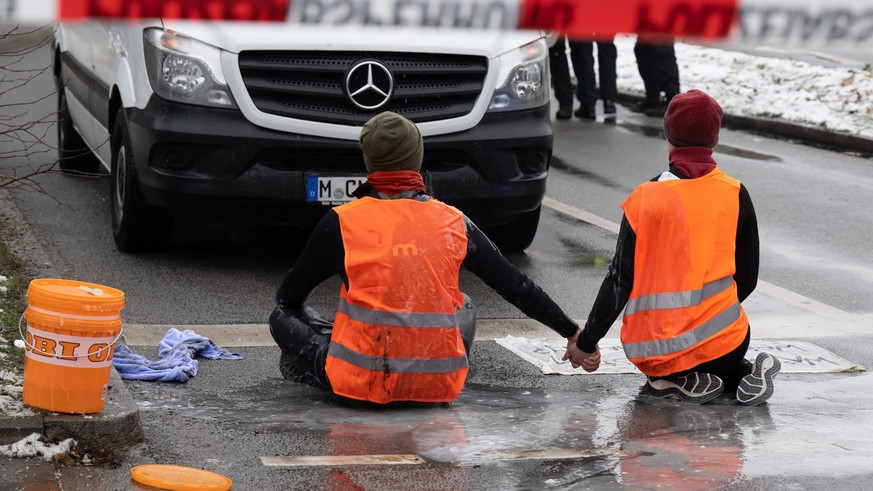 dpatopbilder - 14.12.2022, Bayern, München: Zwei Klimaaktivisten nehmen an einer Protestaktion der Gruppe &quot;Letzte Generation&quot; teil, indem sie versuchen sich auf einer Strasse trotz Nieselreg ...