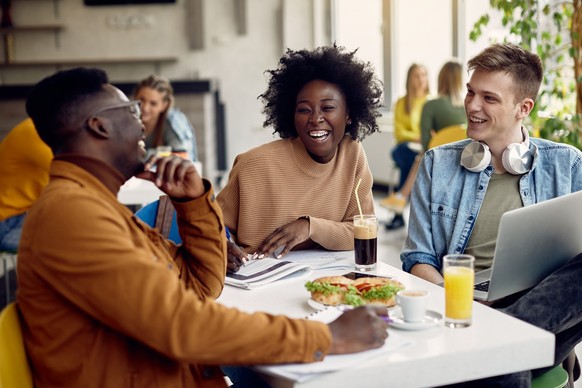 Group of happy students talking while studying at university cafeteria. Focus is on black female student.