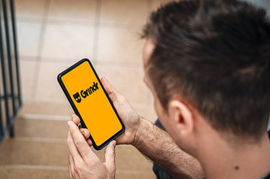 Bavaria, Germany - 22 January 2023: A man with a smartphone in his hand. Grindr dating and sex app or website for homosexuals PHOTOMONTAGE *** Ein Mann mit einem Smartphone in der Hand. Grindr Dating  ...