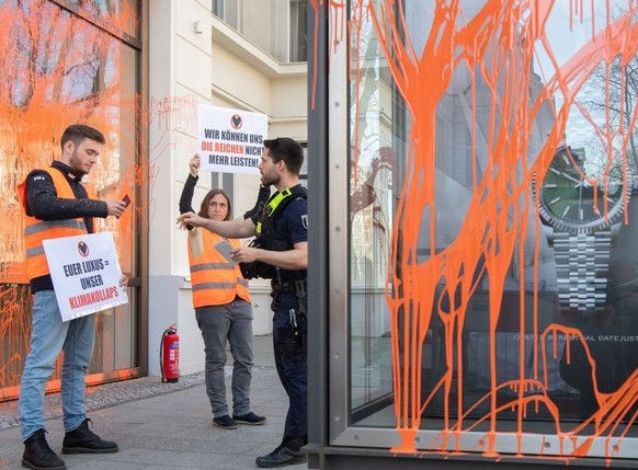 22.04.2023, Berlin: Aktivisten der Umweltschutzgruppe Letzte Generation halten vor einem Luxusgeschäft Plakate. Zuvor hatten sie die Fassade mit Farbe besprüht. Die Polizei nahm nach der Tat die Perso ...