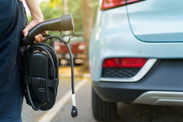 Unrecognizable woman holding the portable EV emergency charging adapter and preparing to charge the EV car. Electric Vehicle charging adapter close up with copyspace.