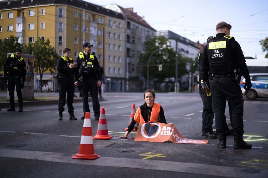 Police officers stand around a climate activist who has glued her hand on a street during a climate protest in Berlin, Germany, Friday, May 19, 2023. Activists of the &quot;Last Generation&quot;, Letz ...