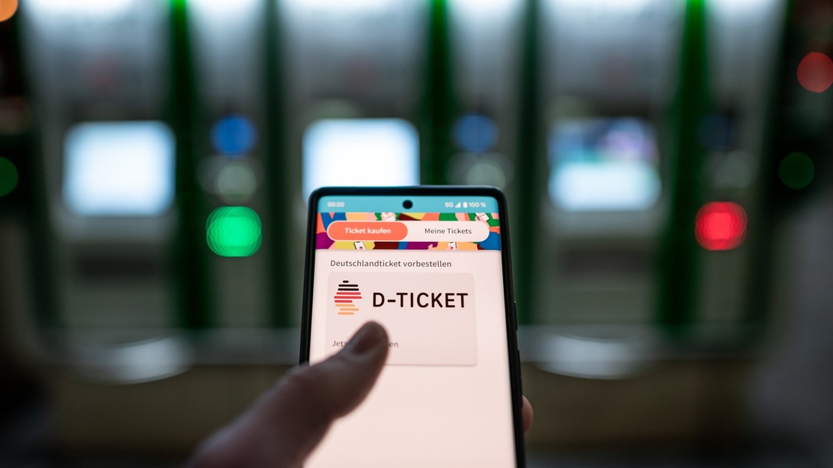 ARCHIV - 03.04.2023, ---: Ein Mann hält ein Mobiltelefon, auf dem das «D-Ticket» gekauft werden kann, vor Ticketautomaten am Hauptbahnhof in der Hand. (zu dpa: «Bayern: Bund muss Zusagen bei Deutschla ...