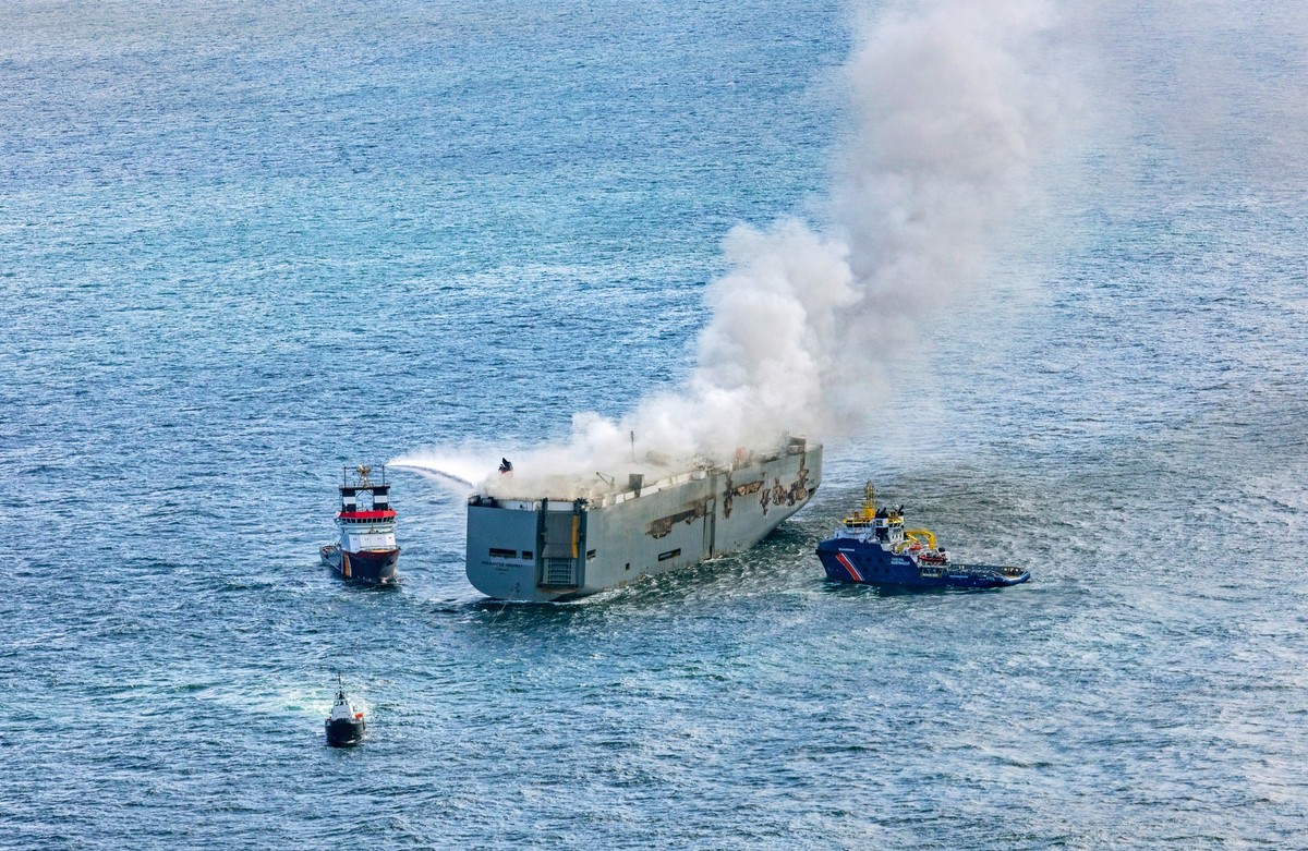 26.07.2023, Niederlande, Ameland: Eine Luftaufnahme zeigt den deutschen Notschlepper "Nordic" (l), der das Feuer auf einem brennenden Frachter in der Nordsee bekämpft. Rechts ist das Boot &q ...