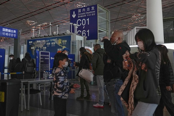 29.12.2022, China, Peking: Passagiere mit Mund-Nasen-Schutz stehen am Flughafen Peking an der Sicherheitskontrolle vor einem internationalen Abfluggate an. Vorstöße der USA, Japans und anderer Länder, ...