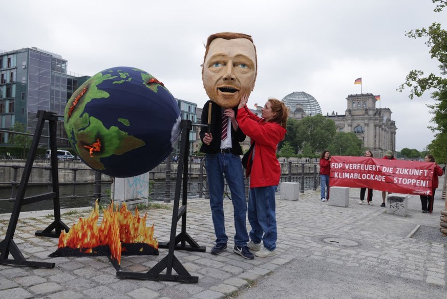 BERLIN, GERMANY - MAY 23: An activist dressed as German Finance Minister and leader of the German Free Democrats (FDP) Christian Lindner gets a little help before spinning a globe over a mock fire as  ...
