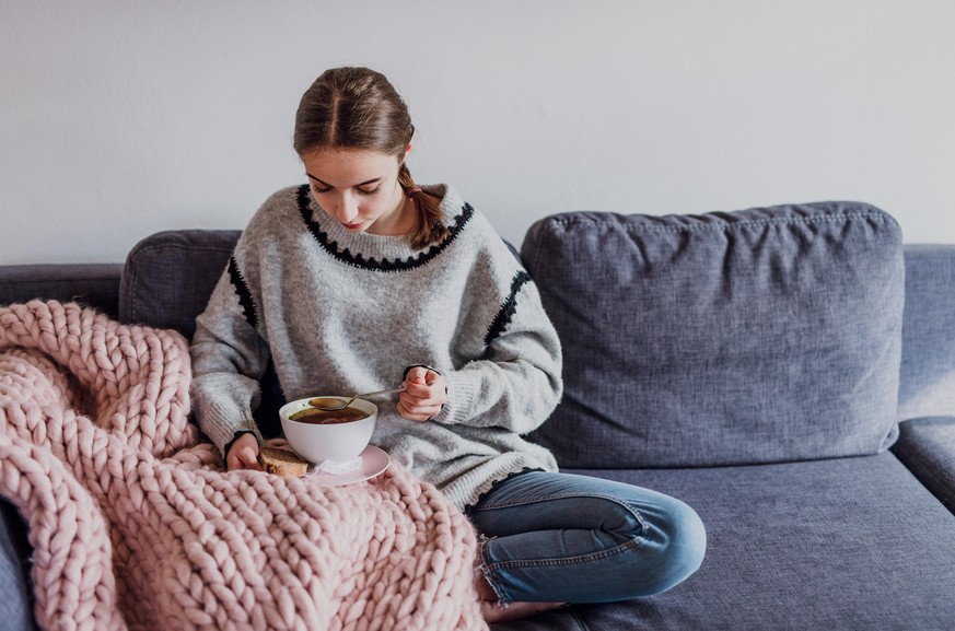 junge Frau sitz auf Sofa und isst Suppe (Foto: picture alliance / Mikelo / VisualEyze) || Modellfreigabe vorhanden