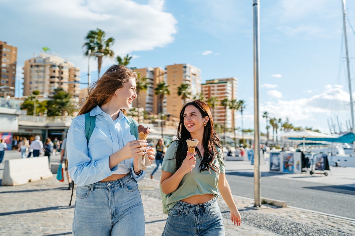 Two beautiful female friends eating an ice cream while walking on the quayside in Málaga in Spain.