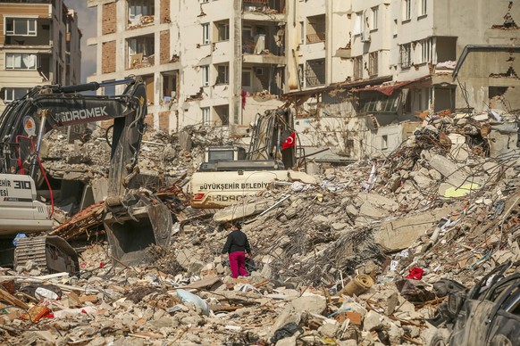 22.02.2023, Türkei, Samandag: Ein Mann steht zwischen Trümmern, während Bagger die Überreste eines zerstörten Gebäudes nach dem Erdbeben am 06.02.2023 abreiße. Mehr als 6000 Nachbeben zählte die türki ...