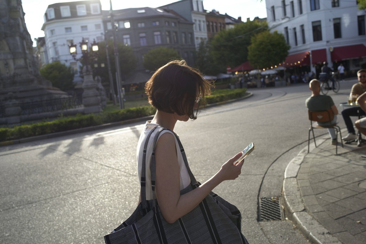 Woman with a bag walks on city street while looking at her phone on a sunny day. Germany bola09228 Copyright: xConnectxImagesx ,model released