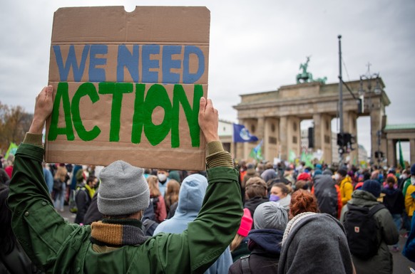 ARCHIV - 22.10.2021, Berlin: Ein Teilnehmer einer Protestaktion der Klimaschutzinitiative «Fridays for Future» steht mit einem Transparent mit der Aufschrift «We need action» vor dem Brandenburger Tor ...