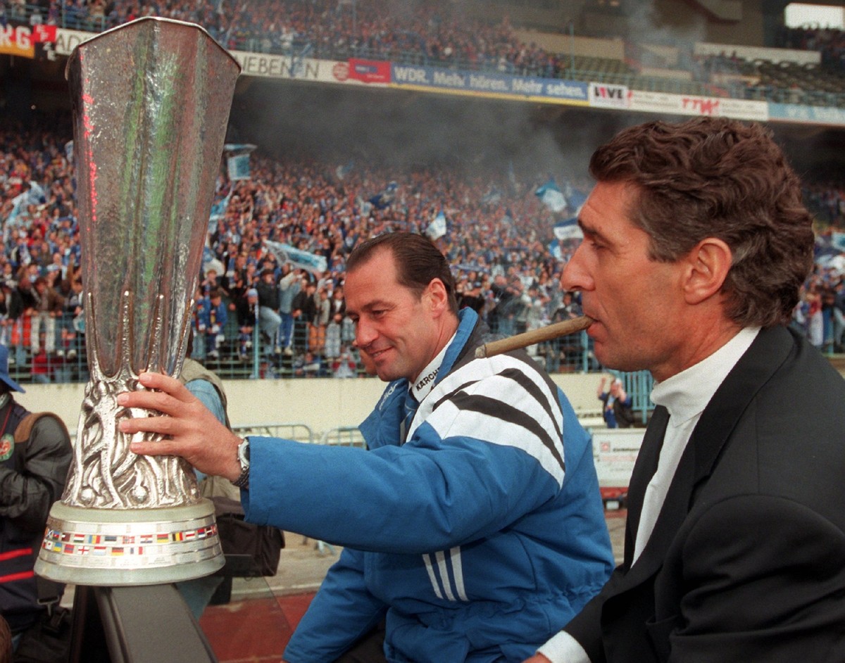 ARCHIV - 22.05.1997, Nordrhein-Westfalen, Gelsenkirchen: Der Trainer des FC Schalke 04, Huub Stevens (l) h�lt im Gelsenkirchener Parkstadion den UEFA-Pokal fest in der Hand, neben ihm der Manager Rudi ...