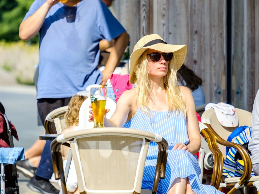 Moscow. Russia. June 26, 2021. A young blonde woman drinks light beer from a glass at a table of a street cafe. Summer sunny day in the city. The woman is wearing a wide-brimmed hat and sunglasses. xk ...