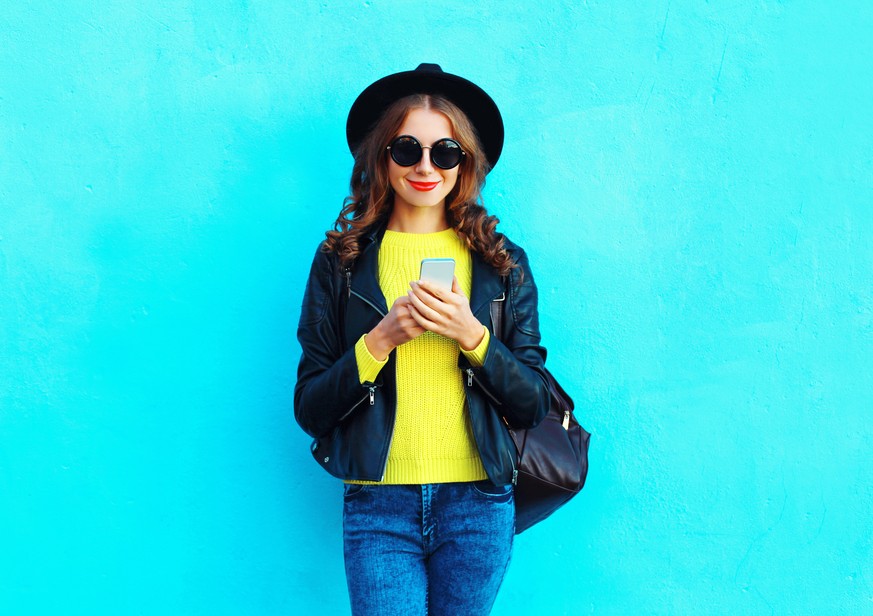 Fashion pretty woman using smartphone wearing a black rock style clothes over colorful blue background