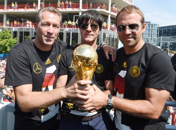 ARCHIV - 15.07.2014, Berlin: Der damalige Torwarttrainer Andreas Köpke (Deutschland, l-r), damaliger Bundestrainer Joachim Löw (Deutschland) und Hansi Flick (Deutschland) halten bei der Feier der deut ...