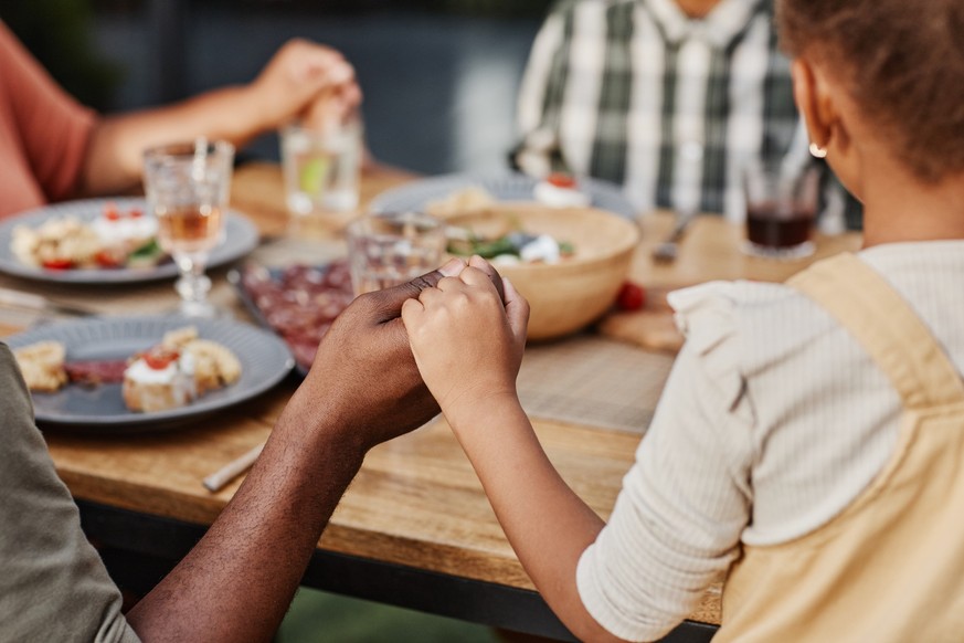 Close up of children holding hands at family dinner outdoors and praying, copy space