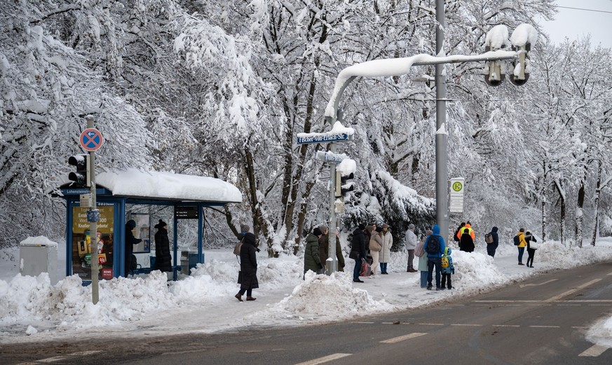 04.12.2023, Bayern, München: Fahrgäste warten an einer verschneiten Haltestelle auf einen Bus. Foto: Lukas Barth/dpa +++ dpa-Bildfunk +++