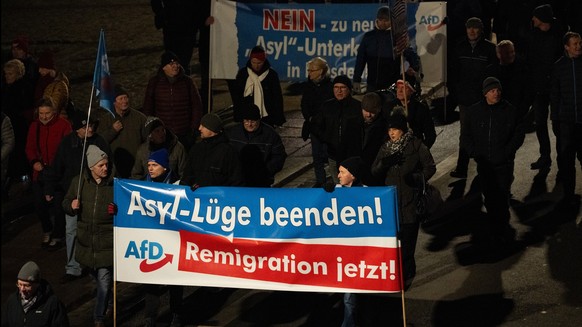ARCHIV - 18.12.2023, Sachsen, Dresden: Teilnehmer einer Demonstration der rechtsextremistischen Bewegung Pegida laufen am Abend am Terrassenufer entlang und tragen Banner der AfD mit der Aufschrift &q ...
