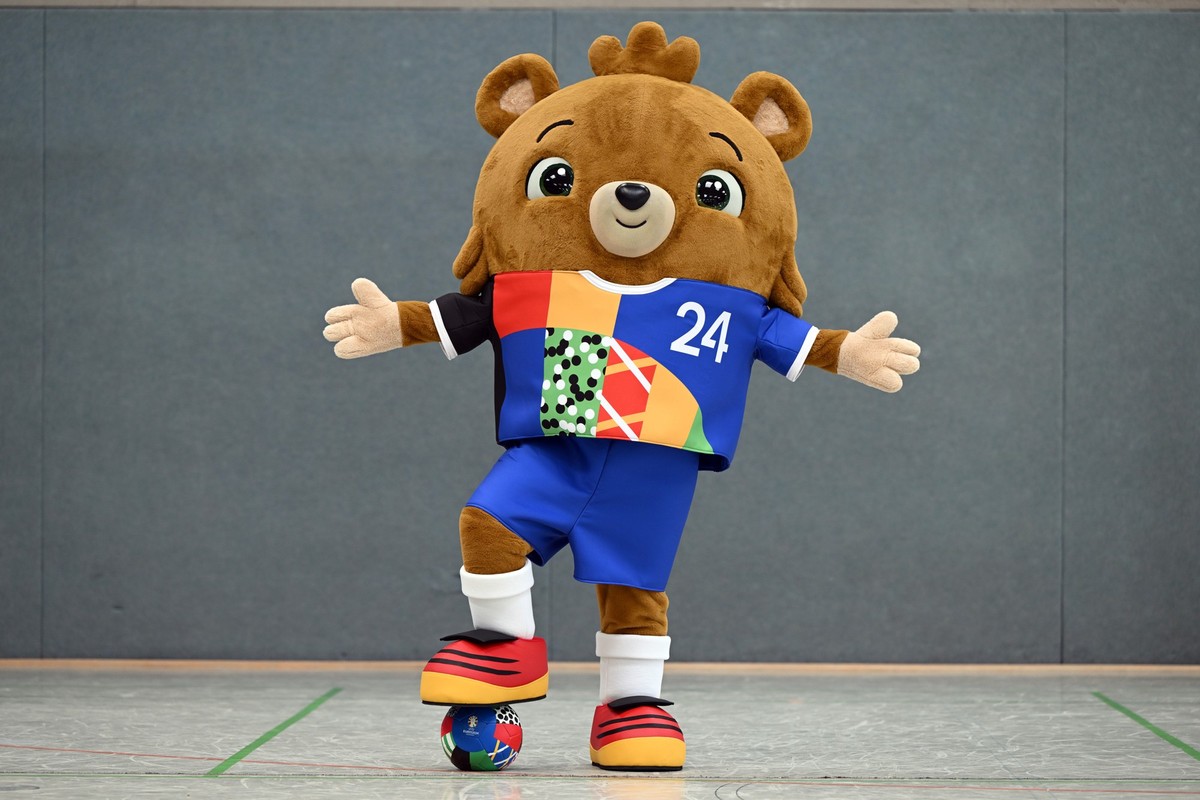 20.06.2023, Nordrhein-Westfalen, Gelsenkirchen: Fußball: EM 2024, Vorstellung des offiziellen Maskottchens. Das noch namenlose Maskottchen steht in einer Sporthalle. Ein putziger kleiner Bär - mit Hos ...
