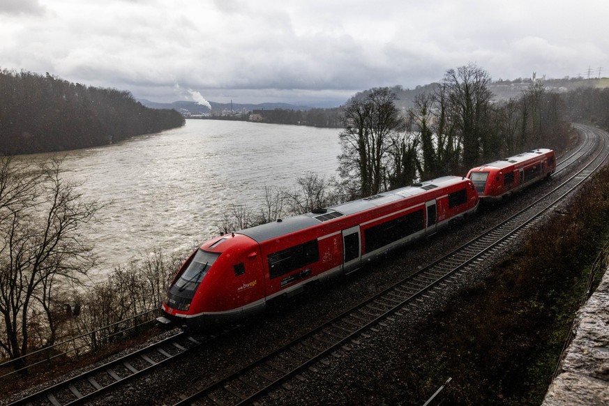 PRODUKTION - 14.12.2023, Baden-Württemberg, Rheinfelden: Ein Zug fährt auf der Strecke der Hochrheinbahn zwischen Basel und Erzingen. Im Hintergrund fließt der Rhein. Die kommende Unterzeichnung des R ...