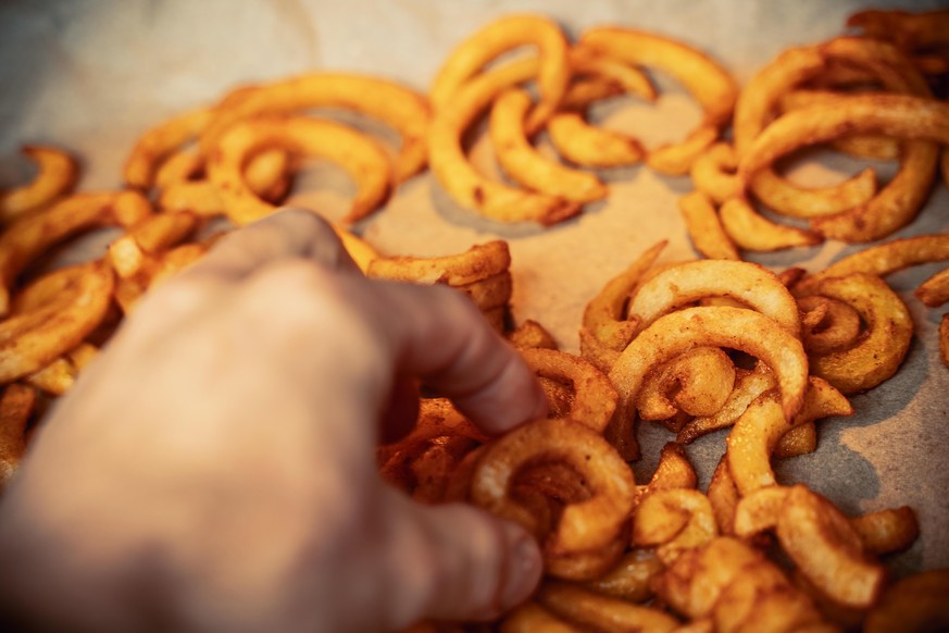 gelockte Pommes aus Kartoffeln in einem Backofen zuhause gebacken, schnelles ungesundes Fertiggericht aus dem Ofen in der Küche gebacken auf Backpapier - Curly Fries