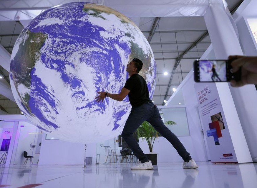 An attendee poses for a picture near a model earth during the COP27 climate summit in Sharm el-Sheikh, Egypt November 19, 2022. REUTERS/Mohamed Abd El Ghany