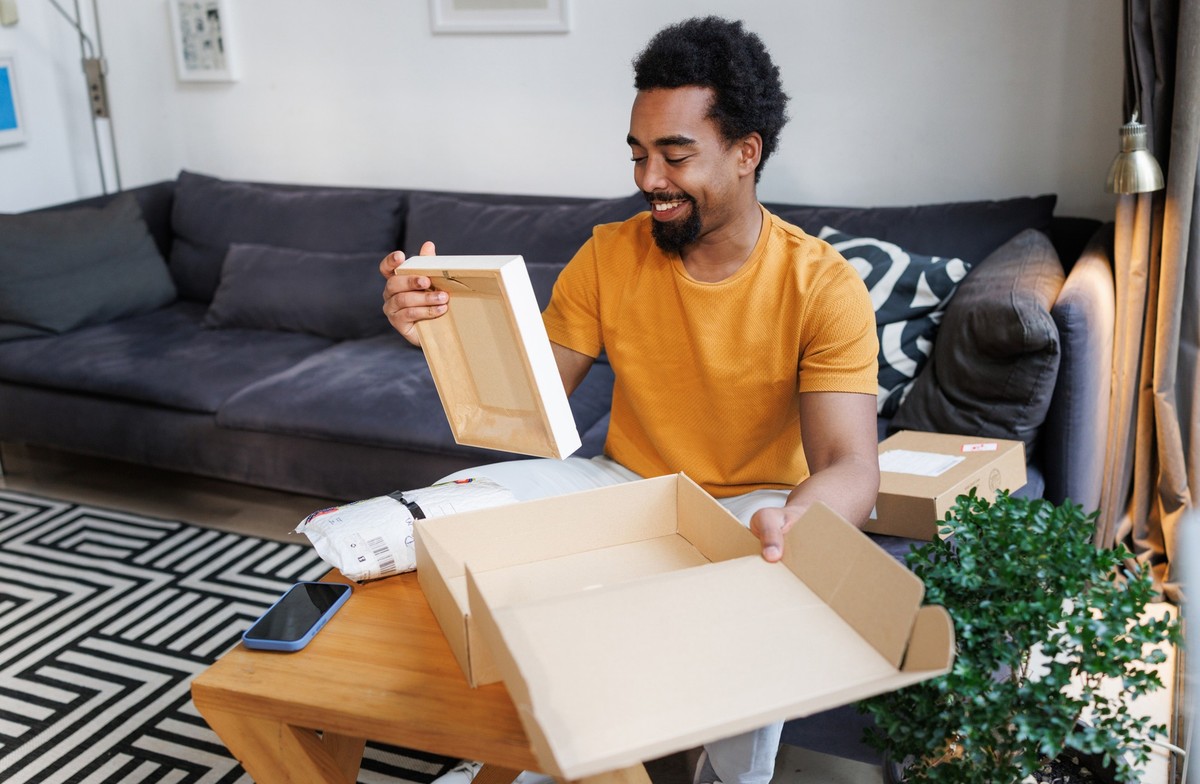 A cheerful man in a casual setting happily opens packages, enjoying his deliveries.