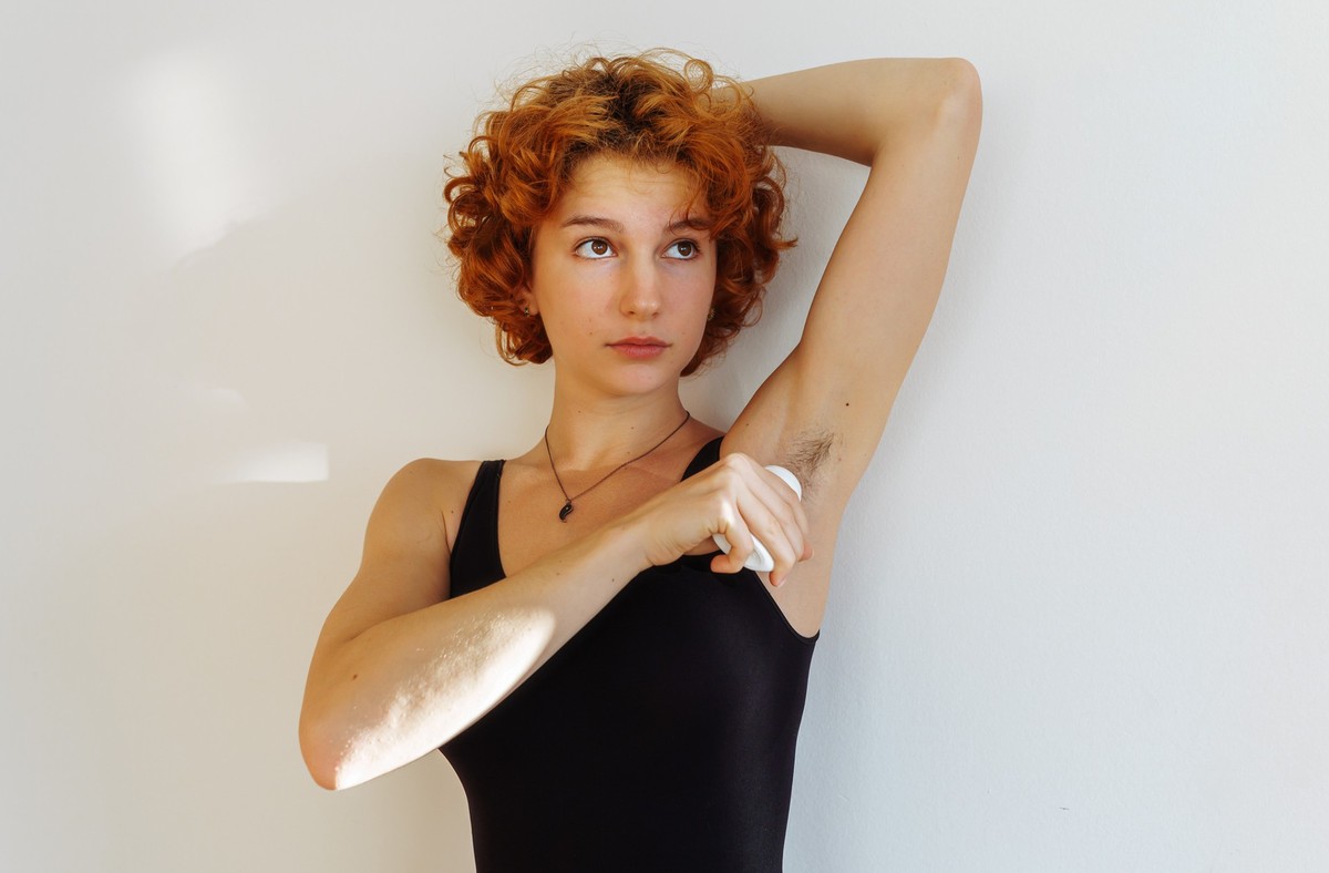 young woman uses hygiene product, roll-on deodorant, antiperspirant, against sweat odor, applies product to unshaven armpits