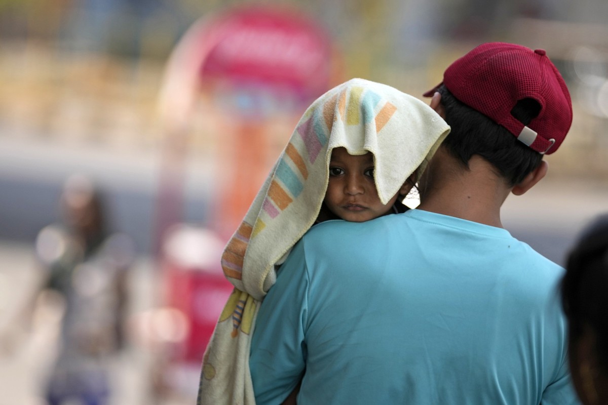 02.06.2024, Indien, Jammu: Ein Mann trägt ein Kind, dessen Kopf mit einem Handtuch bedeckt ist, um es vor der Hitze zu schützen. Foto: Channi Anand/AP/dpa +++ dpa-Bildfunk +++