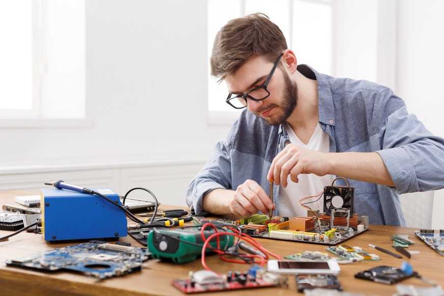 Repairman disassembling computer motherboard with screwdriver. Engineer fixing computer circuit in electronics repair service, copy space