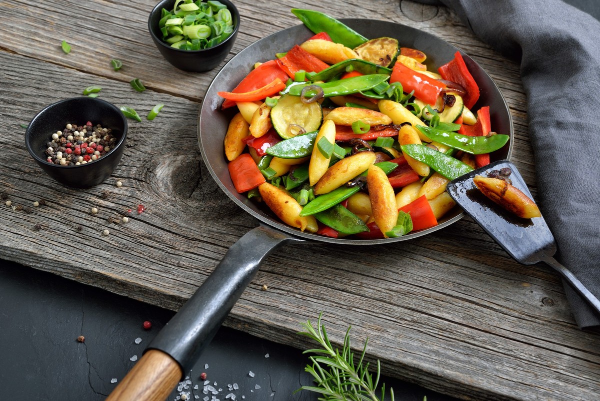 Roasted vegan finger-shaped potato dumplings with fresh vegetables in an iron frying pan