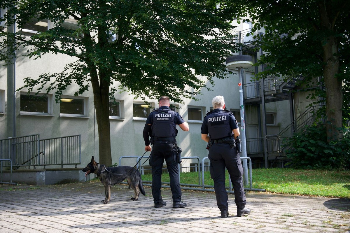 19.07.2024, Schleswig-Holstein, Wedel: Mitarbeiter der Polizei stehen bei einer Schule in Wedel. Auf dem Gelände einer Volkshochschule in Wedel bei Hamburg ist eine Lehrkraft niedergestochen worden. F ...